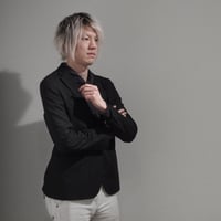 写真： 半田のプロフィール写真。髪が白めで腕を組んで右を向いている